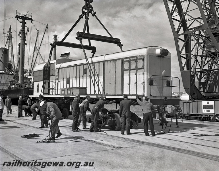 P15045
English Electric H class diesel loco being unloaded, body being lowered by crane onto bogies, workers, North Quay, Fremantle Port, side and front view, c1966
