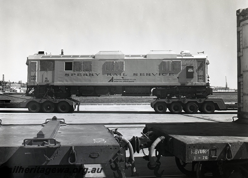 P15051
Sperry Rail Service railcar 140, on road transport trailer, in middle distance, side view, in foreground the coupling mechanism between a flat top wagon with WAGR plate and 