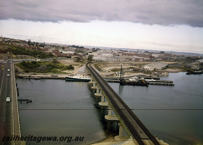 P15063
Newly constructed rail bridge over Swan River, concrete and steel, road bridge, ships docked, town and ocean in background, Fremantle, ER line, c1965
