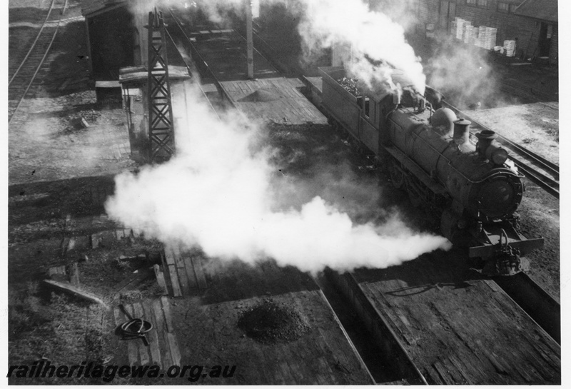P15123
ESL class 328 steam locomotive at Katanning Loco depot. Overhead view from coal stage showing ash pits in foreground and portion of shed in background. GSR line.
