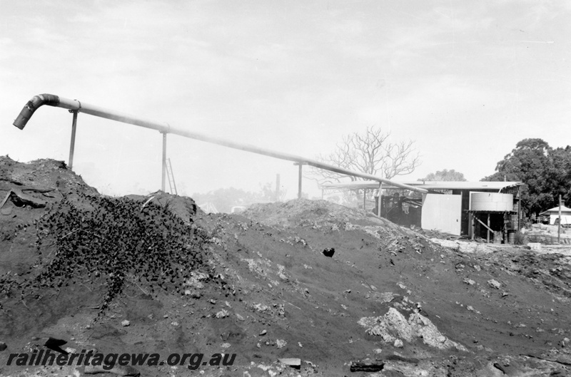P15175
3 of three views of the sleeper mill located trackside at Narrikup, c1970/71, GSR line, roadside view of the sawdust dump with a long discharge pipe emanating at the mill
