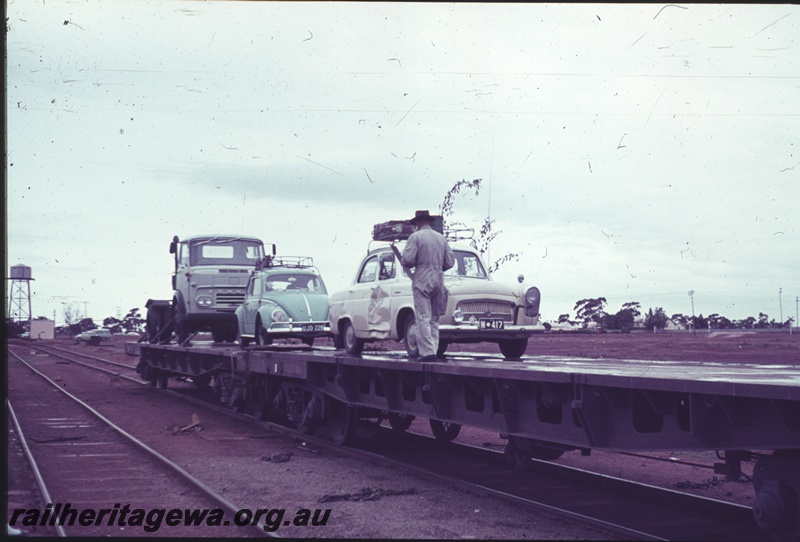 P15207
Motor vehicles being loaded onto Commonwealth Railways (CR) wagons, Parkeston, TAR line, water tower in the background
