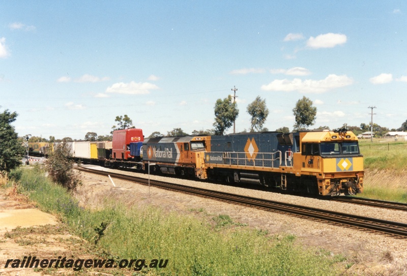 P15512
National Rail NR class 39 and DL class 49, in the orange and grey livery head a freight train northwards through Hazelmere at 11.30 am, a double decker bus is on the first wagon behind the locos, view along the train
