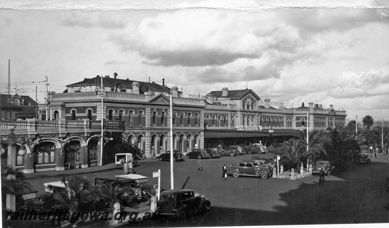 P15623
Station building, Perth, forecourt looking east with road vehicles parked in front of the building
