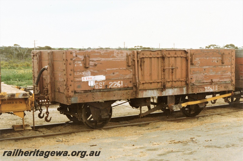 P15729
GST class 2261 four wheel medium sided wagon with ends of floor planking visible, brown livery but with a yellow brake arm, Dowerin, GM line, end and brake lever side view.
