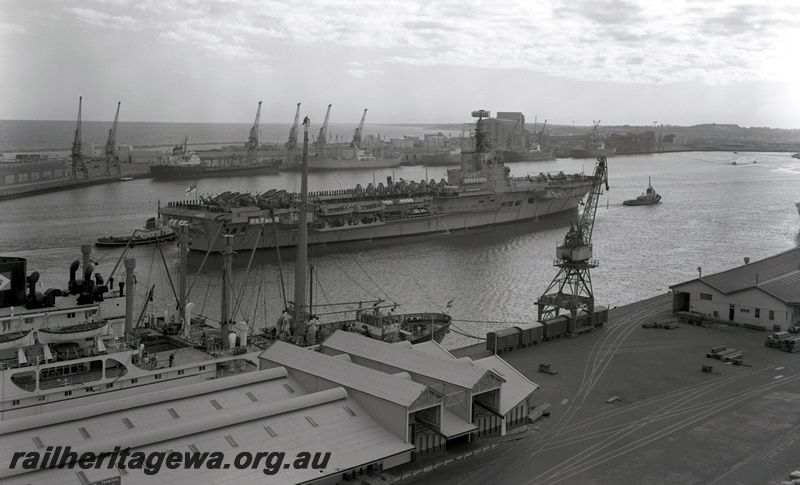 P15859
Vans under a crane, tracks entering wharf, Victoria Quay, Fremantle Harbour, aircraft carrier, HMS Albion seen arriving at Fremantle, elevated view across the harbour.
