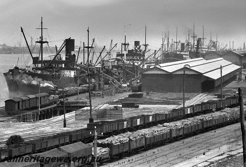 P15861
Rake of wagons loaded with bagged wheat and a rake of empty wagons, shops being loaded with bagged wheat with loaded wagons being shunted along the wharf, North Wharf, Fremantle Harbour. c1934
