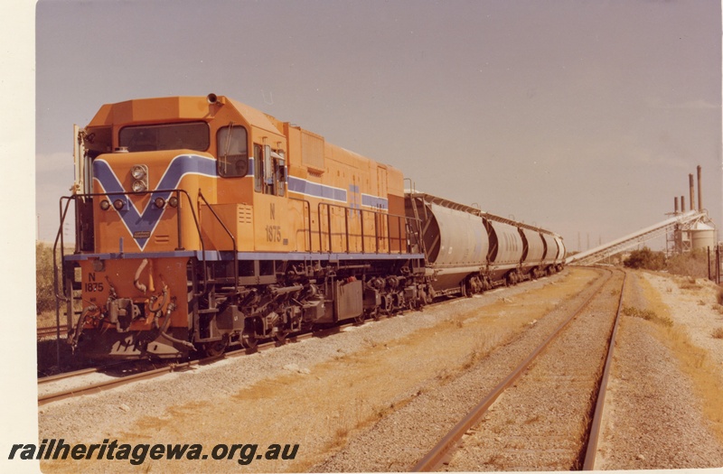 P15899
N class 1875, in Westrail orange with blue and white stripe, on bauxite train, near loading facility, front and side view
