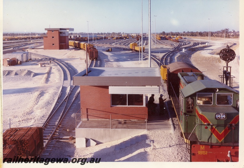 P15905
Forrestfield Yard, control tower, platform and building, M class 1851 in green with red and yellow stripe, assorted wagons, ladder of sidings, hump, view from elevated position
