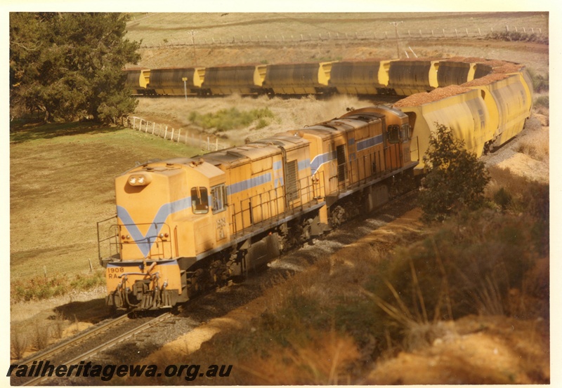 P15910
RA class 1906, in Westrail orange with blue stripe, with another diesel loco, in Westrail orange with blue and white stripe, double heading wood chip train, on a bend in rural setting, front and side view
