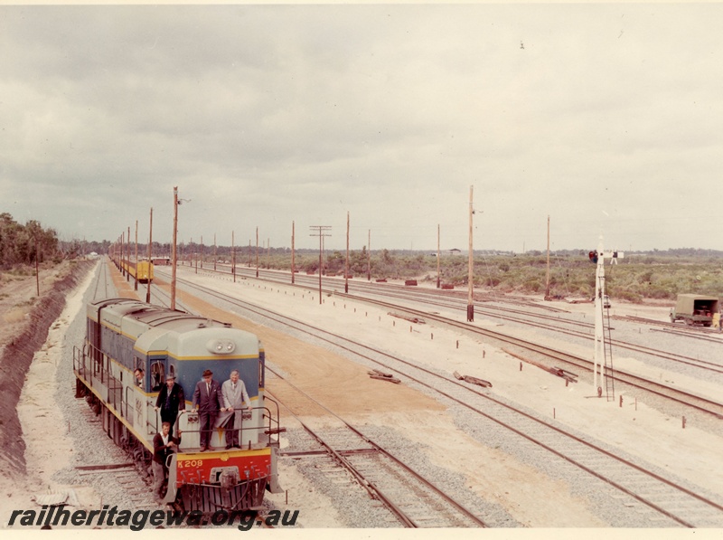 P15914
K class 208, in light blue with blue and yellow stripe, with several men standing on the front, iron ore train, semaphore signal, track laying under way, Kwinana, side and front view from elevated position
