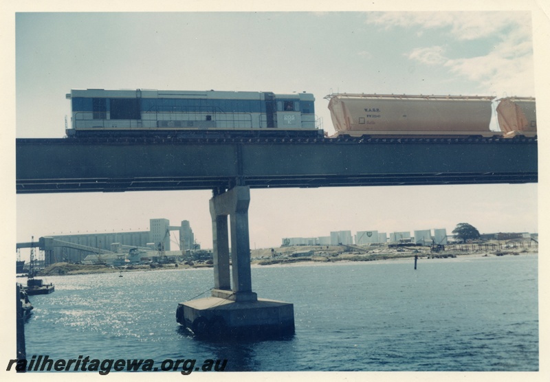 P15917
K class 205, in light blue with dark blue and yellow stripe, on wheat train including wagon WW class 320-40, crossing steel and concrete bridge, Fremantle, side view
