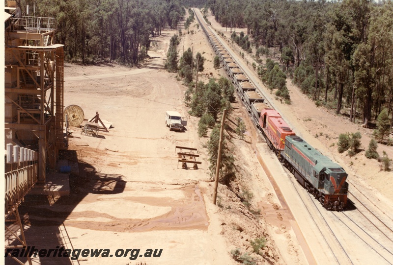 P15925
Two diesel locos, one in green with red and yellow stripe, the other in International safety orange with yellow stripe, double heading bauxite train, Pinjarra, side and front view from elevated position
