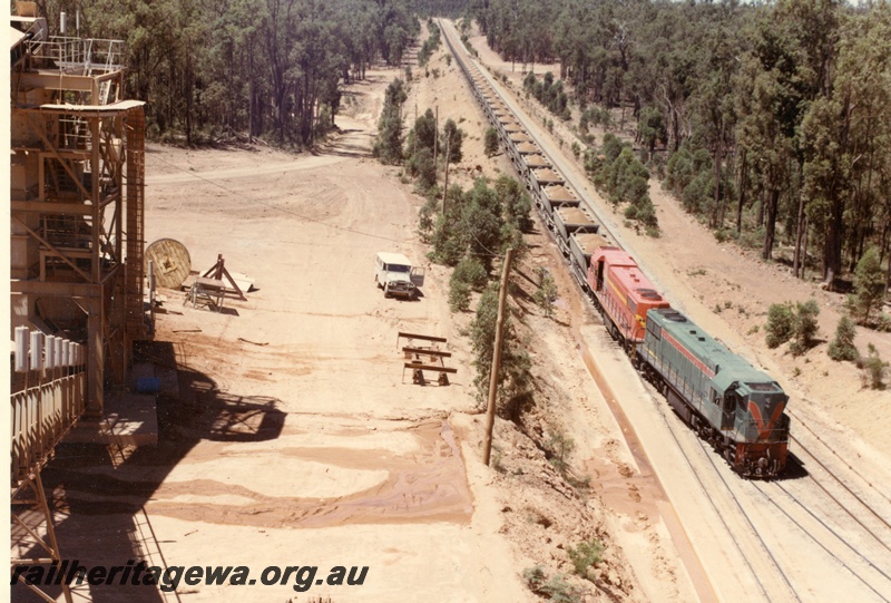 P15925
Two diesel locos, one in green with red and yellow stripe, the other in International safety orange with yellow stripe, double heading bauxite train, Pinjarra, side and front view from elevated position
