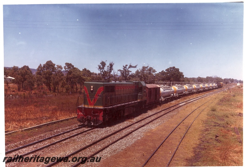 P15936
D class 1562, in green with red and yellow stripe, on caustic train comprising wagons and vans, rural setting, front and side view
