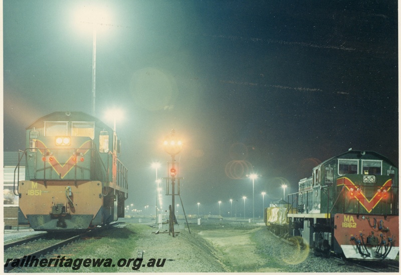 P15950
M class 1851, in green with red and yellow stripe, front view, MA class 1862 also in green with red and yellow stripe, on goods train, side and front view, signal lights, light towers, photo taken at night, Forrestfield Hump Yard 
