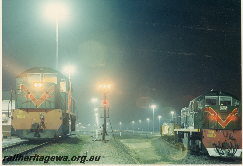 P15950
M class 1851, in green with red and yellow stripe, front view, MA class 1862 also in green with red and yellow stripe, on goods train, side and front view, signal lights, light towers, photo taken at night, Forrestfield Hump Yard 
