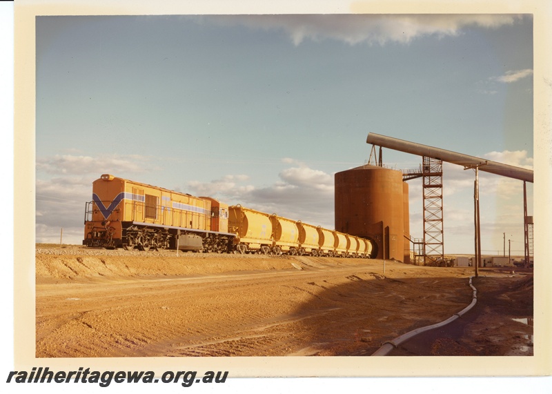 P15966
RA class 1907, in Westrail orange with blue and white stripe, on mineral sands train, being loaded at Eneabba, loader, XE line class wagons, front and side view

