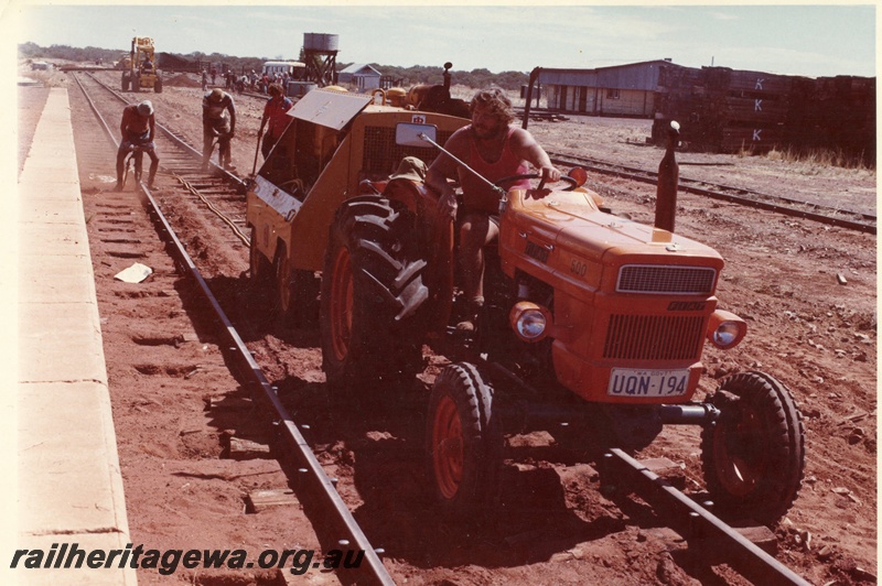 P15993
Regauging standard gauge track, edge of platform, workers, front end loader, Fiat 500 tractor licence no UQN194 with trailer, water tank, trackside buildings, Goongarrie, KL line 
