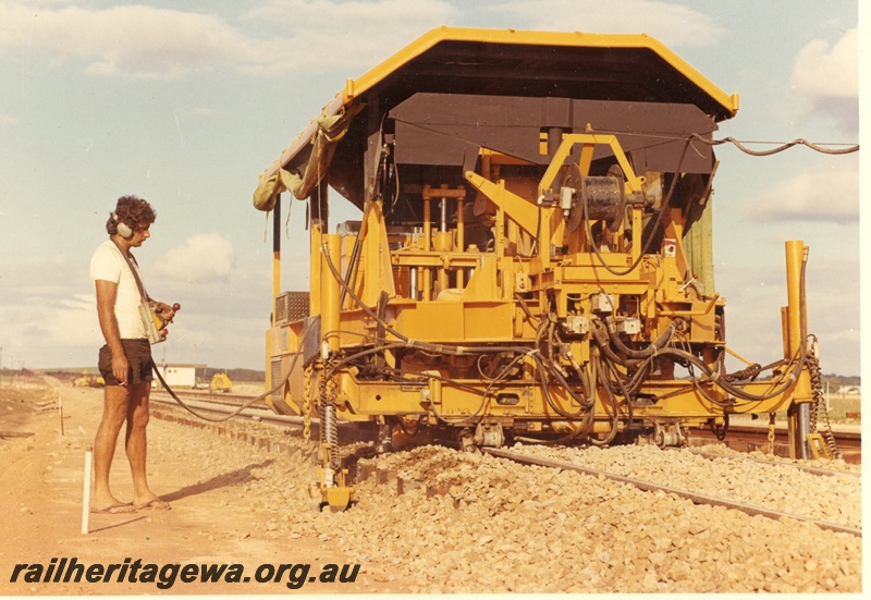 P15998
Mobile track maintenance machine, in yellow colour scheme, being operated by remote control, operator in tee shirt, shorts and thongs, near Dongara bridge, MR line, side and front view
