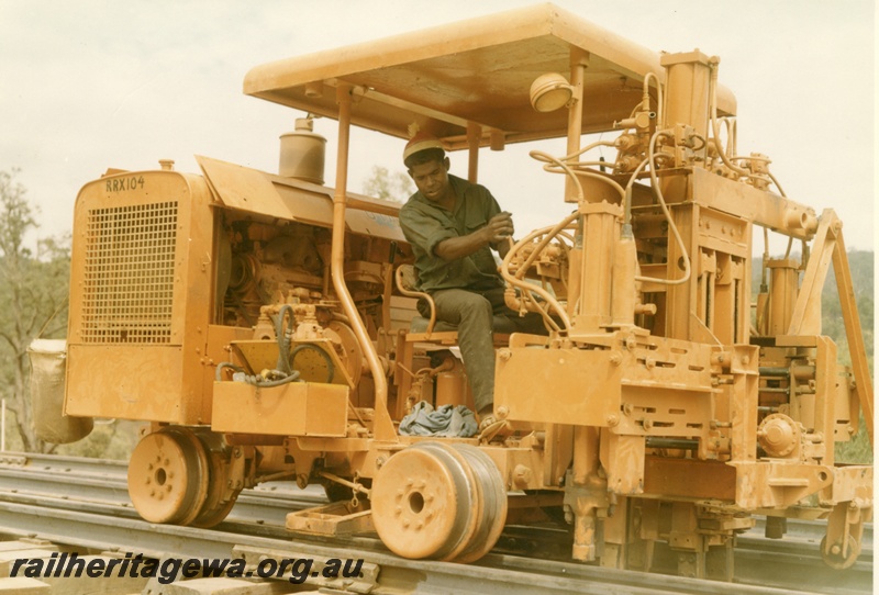 P16011
Motorised track construction trolley, number RRX104, in yellow colour scheme, operator driving, side and front view
