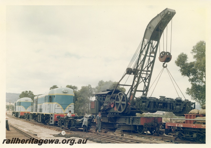 P16022
Breakdown crane no 23, lifting bogie, two diesel locos in light blue with dark blue and yellow stripe livery, bogie on tracks, portion of U class 1730 wagon, view from track level
