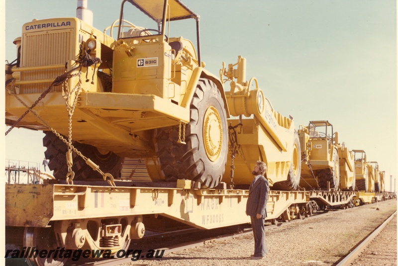 P16027
Rake of flat wagons including WF class 30065, later reclassified as WFCY and others, loaded with Caterpillar earth moving machines, suited onlooker, end and side view from track level
