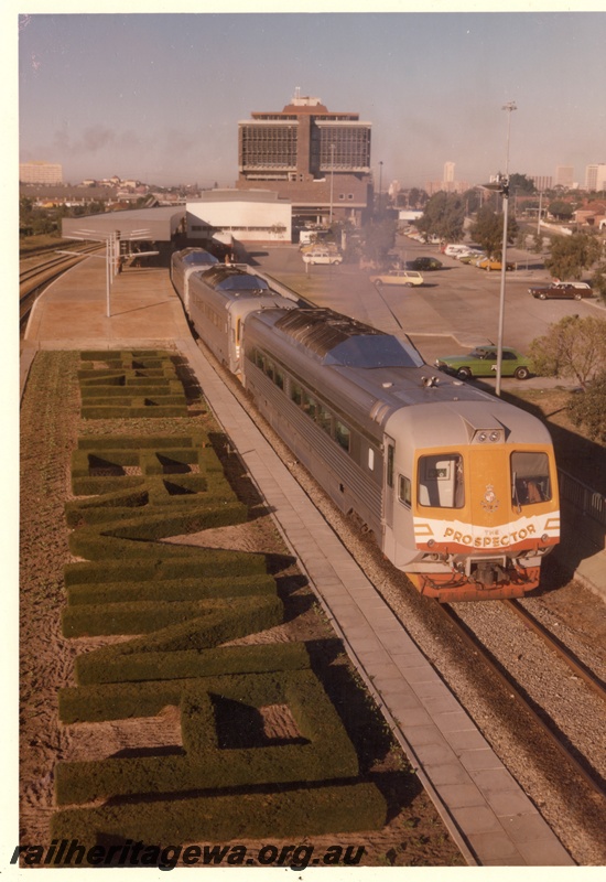 P16069
An overhead view of a three car first series Prospector pictured at Perth Terminal with the temporary Terminal building and the new administrative building in the background. To the left of the lead railcar is the Perth Terminal name set out in shrubs. 
