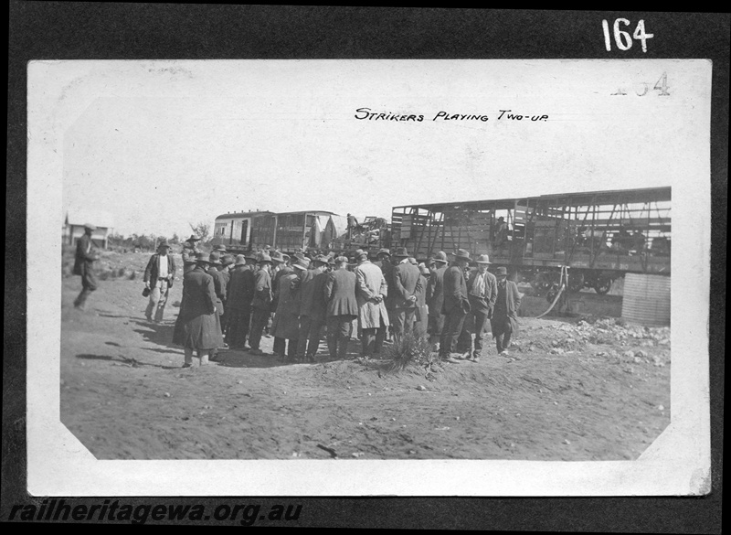 P16177
Commonwealth Railways (CR), rake of carriages including C class 292 cattle wagon and V class 310 sheep wagon, group of strikers playing two up, bush setting, construction of TAR line
