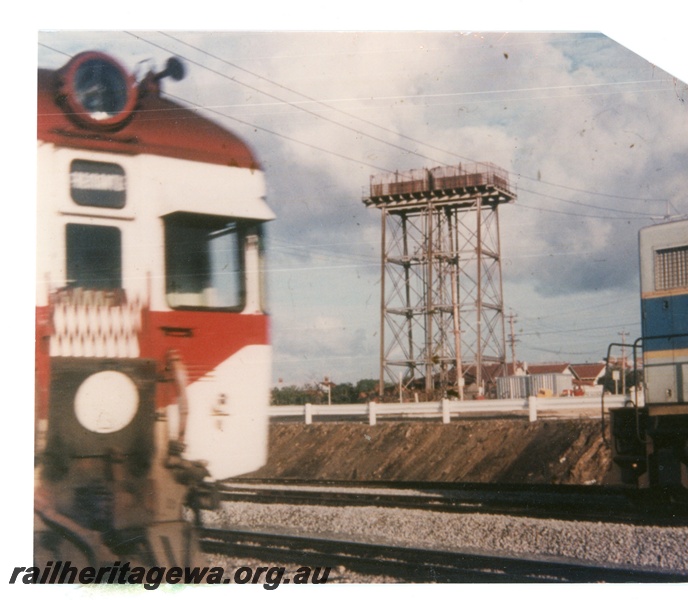 P16312
Water tank, framed between the ends of a railcar and a diesel loco, Summers Street, East Perth, ER line. Tank capacity 50,000 gallons formerly located at Coolgardie.
