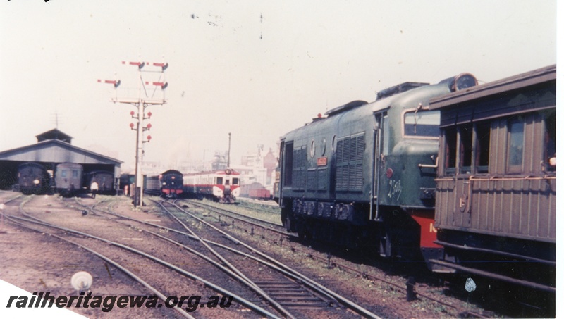 P16348
X class loco in green livery, passenger car (part), D class loco, ADG class railcar set, carriage shed, bracket signal with multiple arms and discs, Perth station yard, ER line, track level view
