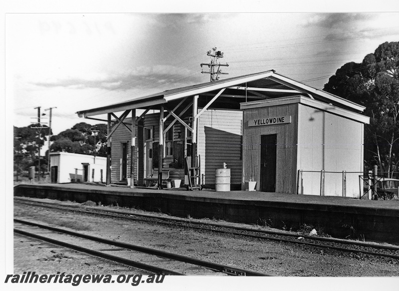 P16699
Station building under an overall canopy roof, Out of Sheds on the platform, another shed at the end of the platform, nameboard,  seat, baggage trolley, Yellowdine, EGR line, view along the platform.
