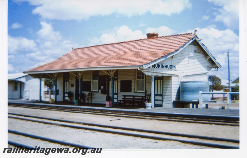 P16701
Station building, weatherboard and tile, another building, platform, seat, plants, scales, hand trolley, water tank, Mukinbudin, WLB line
