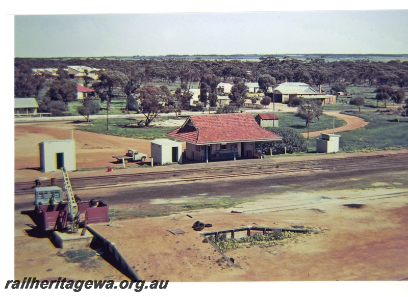 P16703
Overview of Nungarin station, loading ramp with open wagon being loaded, workers, crane, station buildings, town buildings and trees in background, Nungarin, GM line, elevated view from wheat silo
