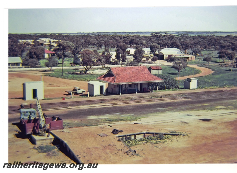 P16703
Overview of Nungarin station, loading ramp with open wagon being loaded, workers, crane, station buildings, town buildings and trees in background, Nungarin, GM line, elevated view from wheat silo
