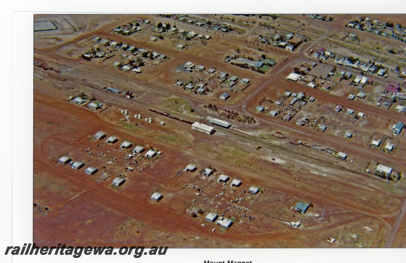 P16707
Town of Mount Magnet, rake of wagons in yard, railway station, goods shed in centre of picture, houses, town buildings, Mount Magnet, NR line, aerial view
