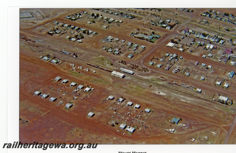 P16707
Town of Mount Magnet, rake of wagons in yard, railway station, goods shed in centre of picture, houses, town buildings, Mount Magnet, NR line, aerial view
