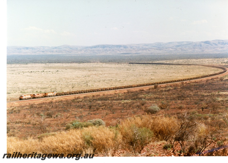 P16764
Mount Newman (MNM) triple headed 180 car loaded ore train at 227 km near Garden loop. Distant view. 
