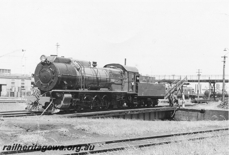 P17045
S class 549 Greenmount on the turntable at East Perth Loco with manual power in operation. An unidentified X class and fuel tanker and footbridge in the background and stores shed to left front of locomotive.
