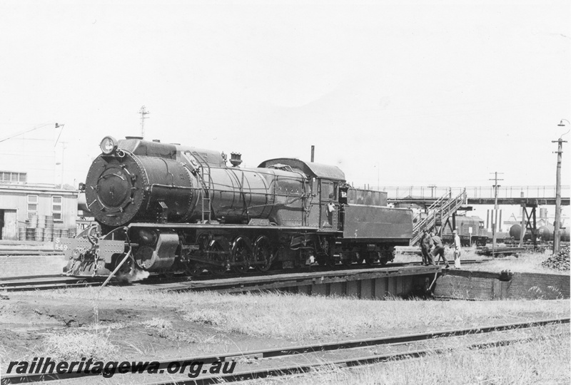 P17045
S class 549 Greenmount on the turntable at East Perth Loco with manual power in operation. An unidentified X class and fuel tanker and footbridge in the background and stores shed to left front of locomotive.
