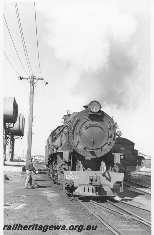 P17088
V class 1206, front view, at East Perth loco. Diesel fuel tanks and power pole to left. Unidentified bunker style loco to right. ER line
