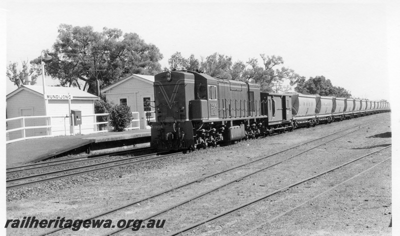 P17136
R class 1904 diesel electric locomotive with a loaded rake of bauxite wagons standing on the loop at Mundijong. Note the station nameboard and buildings to the left of the locomotive and yard trackage in foreground. SWR line.
