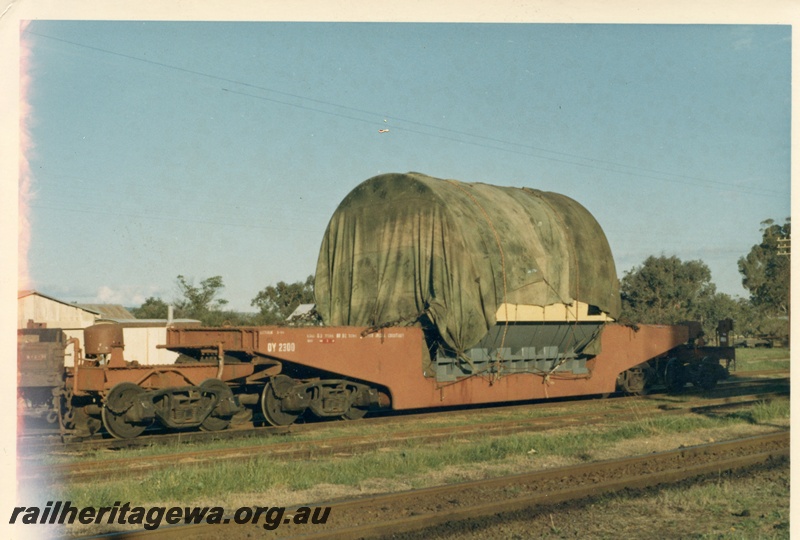 P17159
QY class 2300 heavy lift wagon with a tarpaulin covered load. Location Unknown. Side view of wagon & load. Note the wagon has a total of four bogies necessary for carrying the load.
