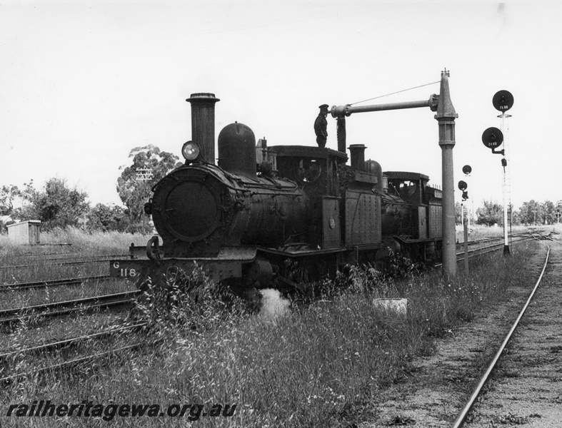 P17258
3 of 4, G class 118 steam locomotive double heading with G class 67 steam locomotive, front and side view, G class 117 taking on water at the water column, searchlight signals, Pinjarra, SWR line. 
