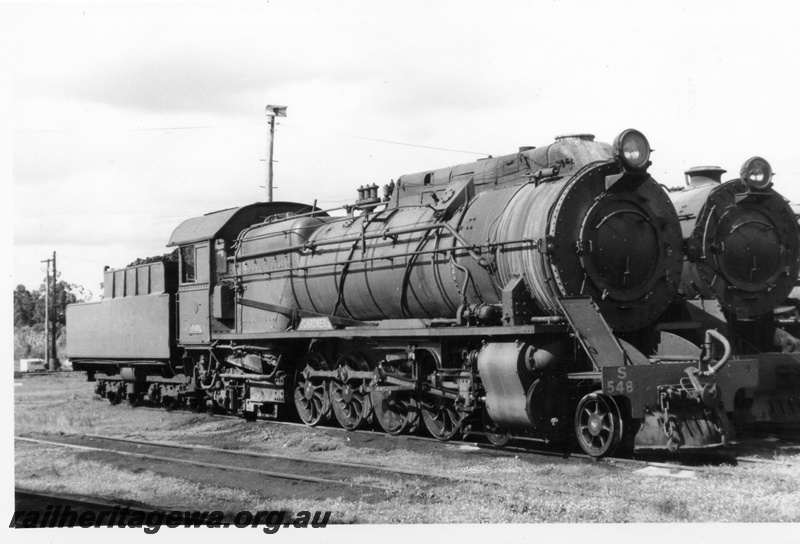 P17450
S class 548 steam locomotive at Collie Depot with an unidentified V class at its side. BN line. Side and front view of locomotive.
