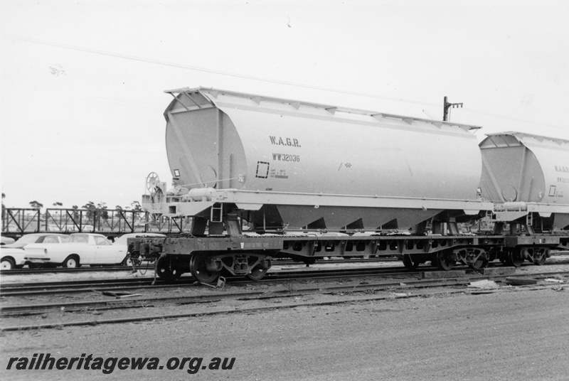 P17845
WW class 32036 loaded on a Commonwealth Railways (CR) flattop wagon at Parkeston prior to unloading to road. In the background are grounded motor vehicles waiting transfer to narrow gauge wagons and the uprights of the standard gauge car transporter wagons. Note the view of the wheat hopper.
