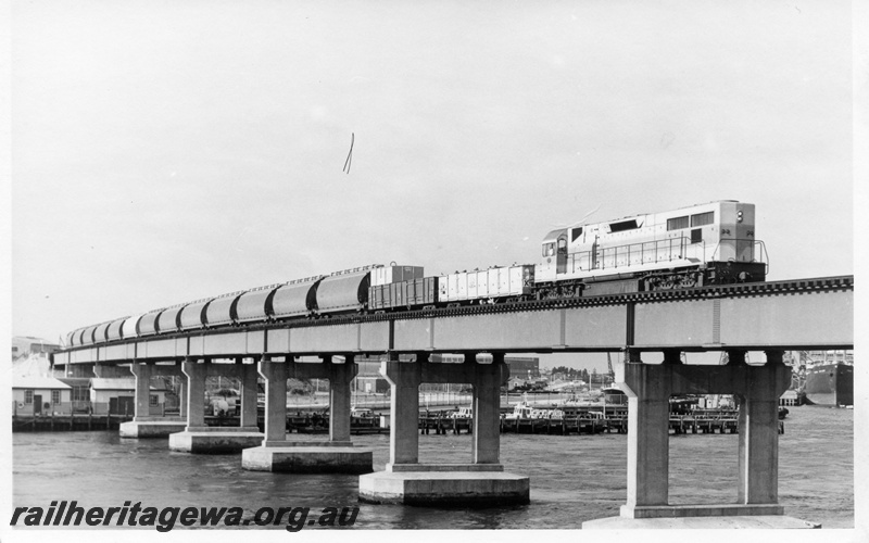 P17899
Diesel hauled goods train, crossing steel and concrete bridge, Fremantle, Swan River, wharves, ship docked, ER line, c1968
