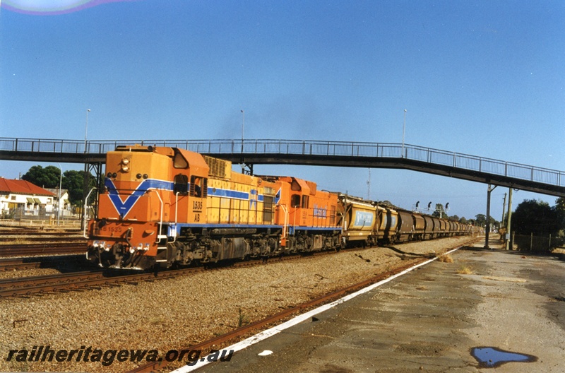 P18041
AB class 1535, AA class 1519, double heading goods train of empty wheat wagons, signal gantry, pedestrian overpass, platform, Midland, ER line 
