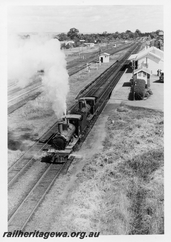 P18206
1 of 3, G class 118 and G class 67 steam locomotives, elevated front view, passing through the station yard, heading north, station buildings, water tower, searchlight signals, Pinjarra, SWR line.
