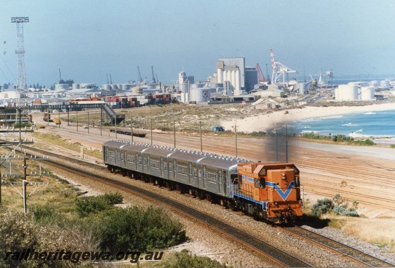 P18308
A class 1511 on 5 car set of Queensland stainless steel carriages, overhead footbridge, beach, port of Fremantle, Leighton yard, ER line 
